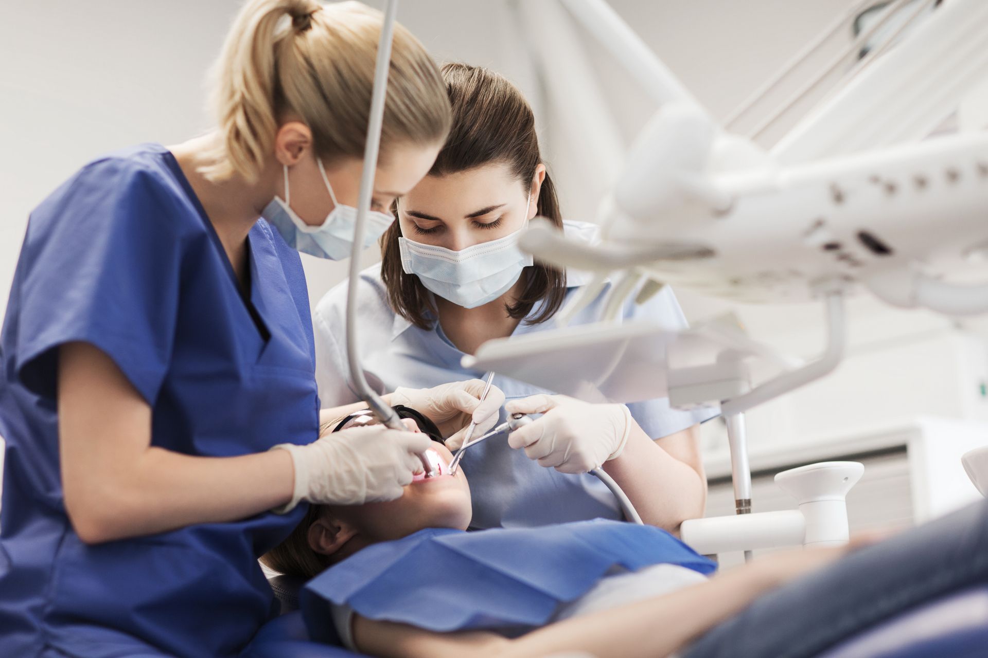 Zahnärzte in blauer OP-Kleidung und mit Masken behandeln einen Patienten in einer Zahnklinik.