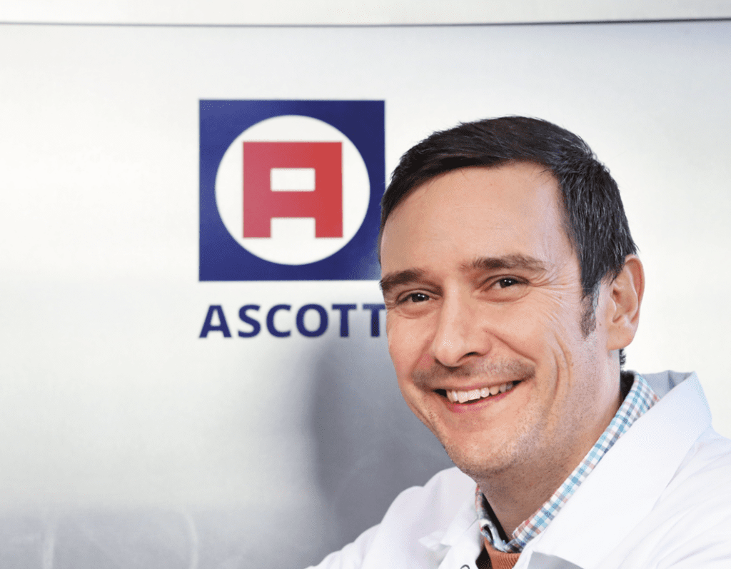 Ein Mann lächelt vor einem ASCOTT®-Logo
