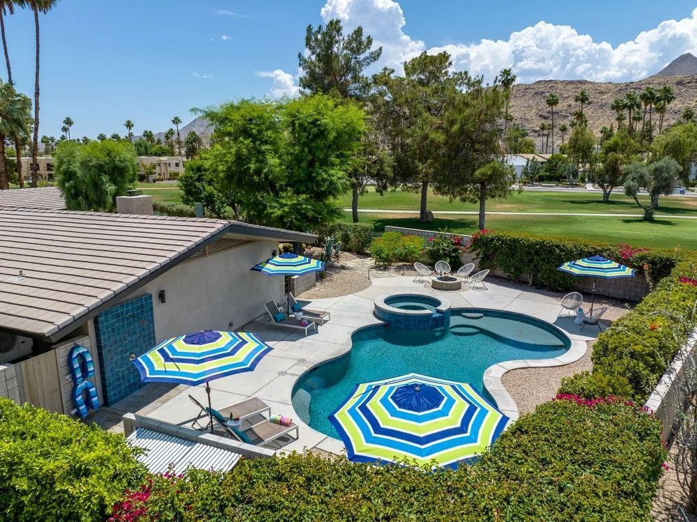 Pool with umbrellas, lounge chairs, and spa surrounded by green bushes and golf course.