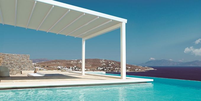 Cochera gris con iluminación LED integrada sobre zona de aparcamiento de hormigón y pequeño jardín.