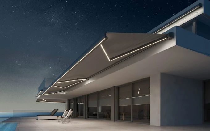 Edificio moderno con toldos iluminados por la noche, con vista a una piscina.