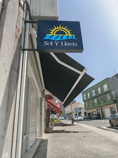 Letrero de la tienda Sol y Lluvia con un sol. Toldo negro sobre la fachada, vista a la calle.