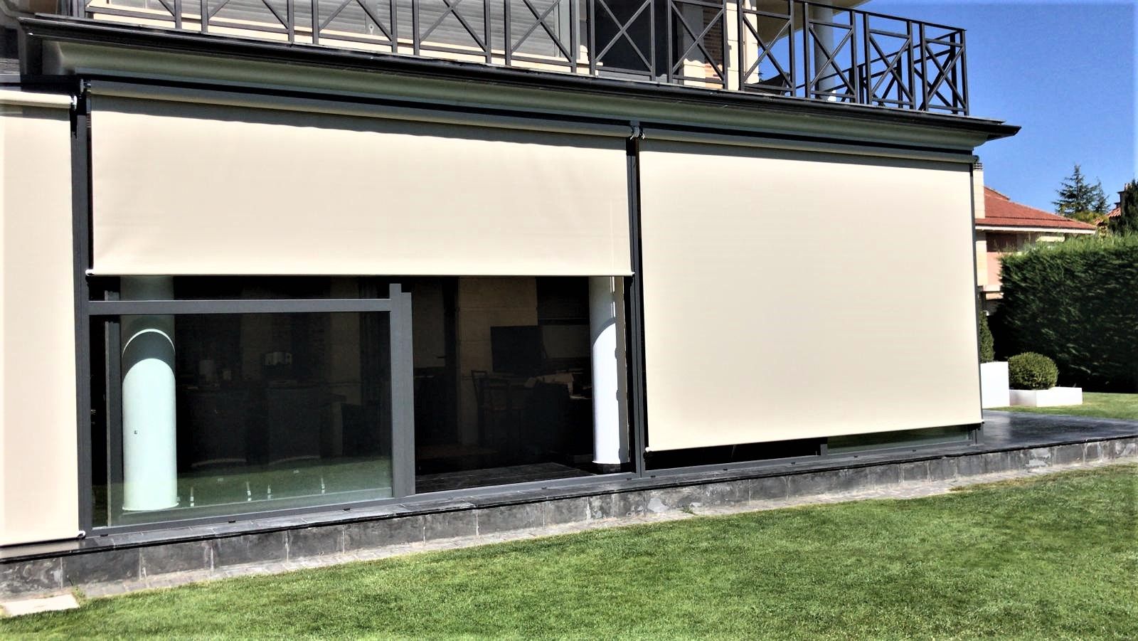 Un toldo de rayas verdes y blancas se extiende sobre un balcón, con vistas a un paisaje urbano bajo un cielo azul.