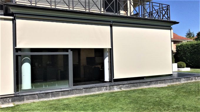 Un toldo de rayas verdes y blancas se extiende sobre un balcón, con vistas a un paisaje urbano bajo un cielo azul.