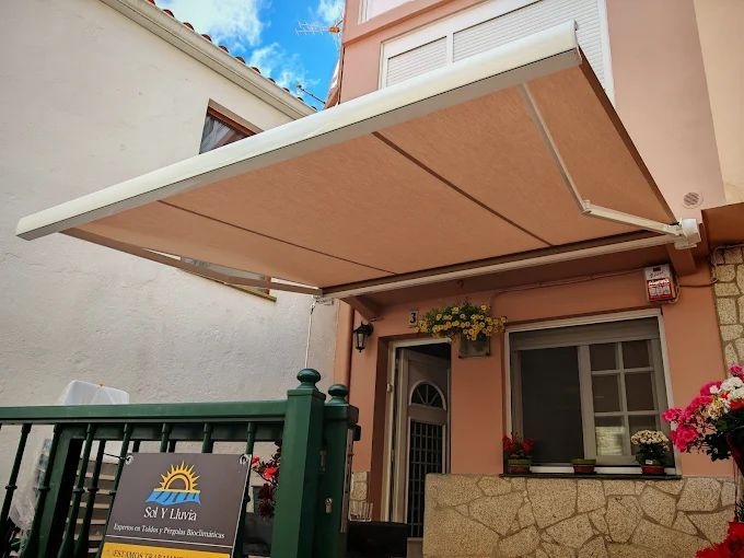 Toldo beige sombreando la entrada de un edificio; fachada rosa claro, barandilla verde, cielo azul.