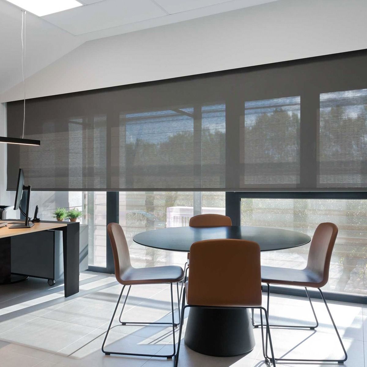 Espacio de oficina moderno con cortinas enrollables de color gris oscuro, mesa redonda y sillas.