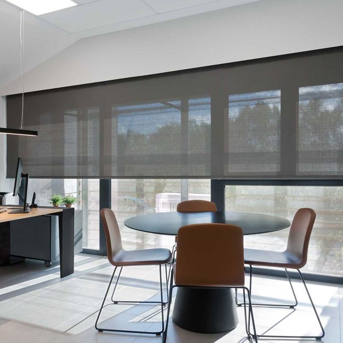 Espacio de oficina moderno con cortinas enrollables de color gris oscuro, mesa redonda y sillas.