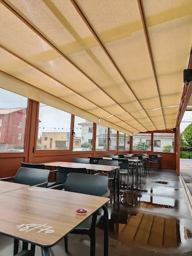 Cafetería al aire libre con mesas y sillas bajo un toldo retráctil; suelo mojado visible.