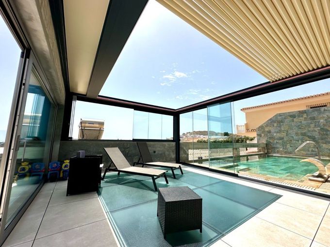 Cochera gris con iluminación LED integrada sobre zona de aparcamiento de hormigón y pequeño jardín.