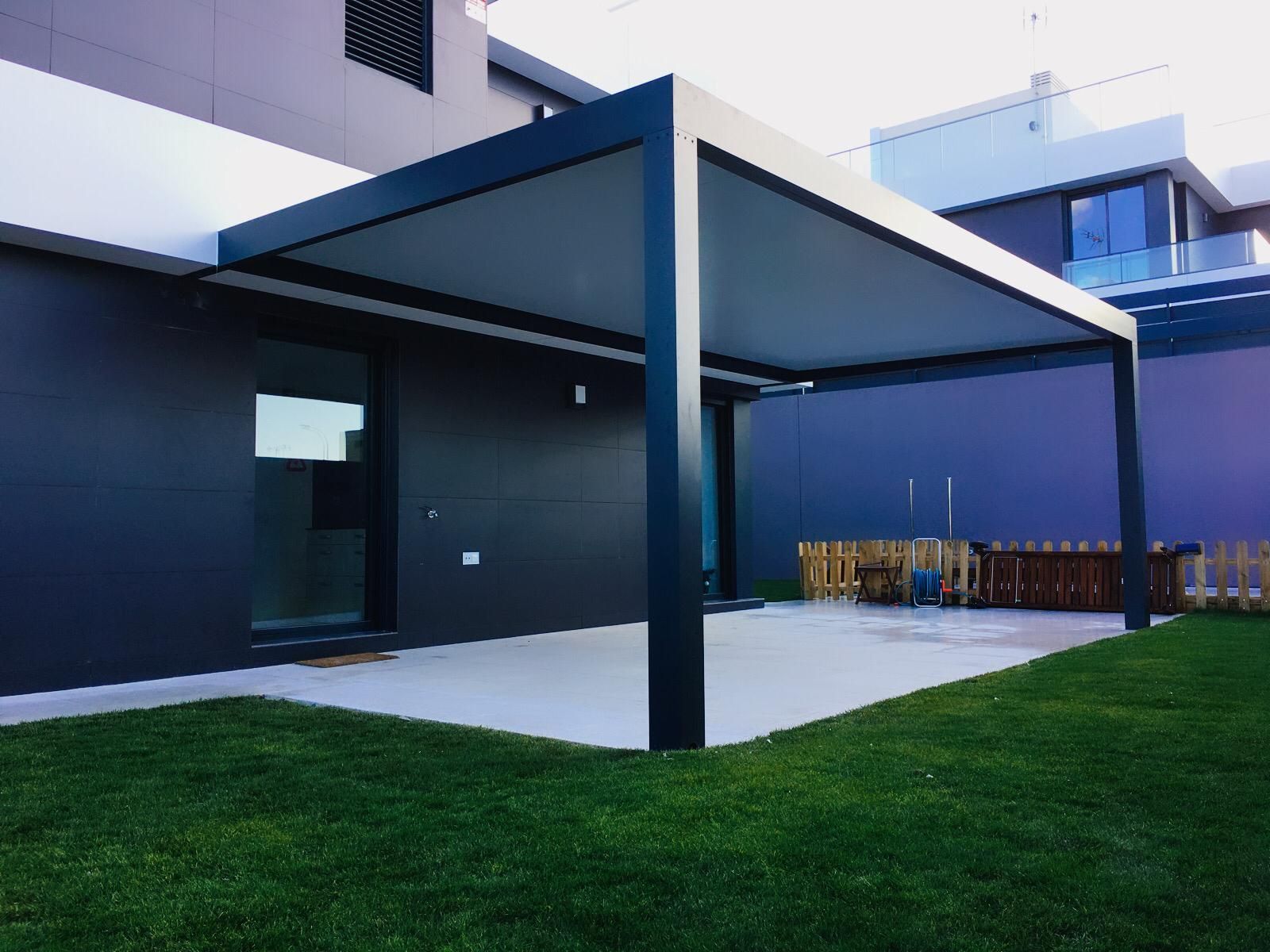 Pérgola con vigas iluminadas sobre un patio con mobiliario, contra un cielo azul crepuscular.
