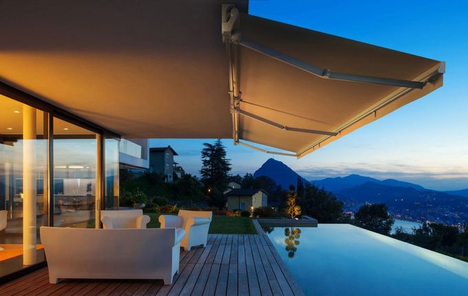 Toldo retráctil negro con luces LED que se extiende desde un edificio, cielo y árboles al fondo.