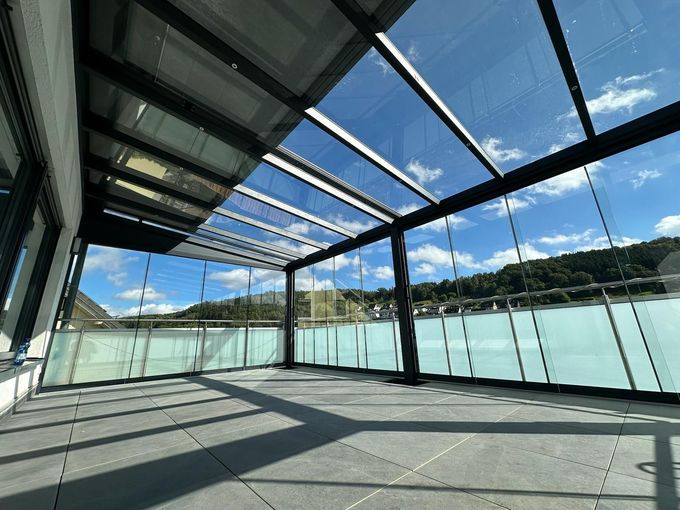 Un toldo de rayas verdes y blancas se extiende sobre un balcón, con vistas a un paisaje urbano bajo un cielo azul.