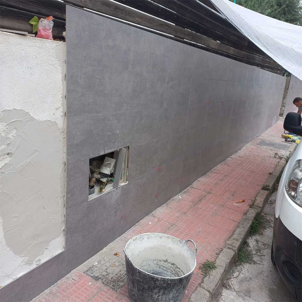 Un hombre está pintando una pared al lado de un cubo de cemento.