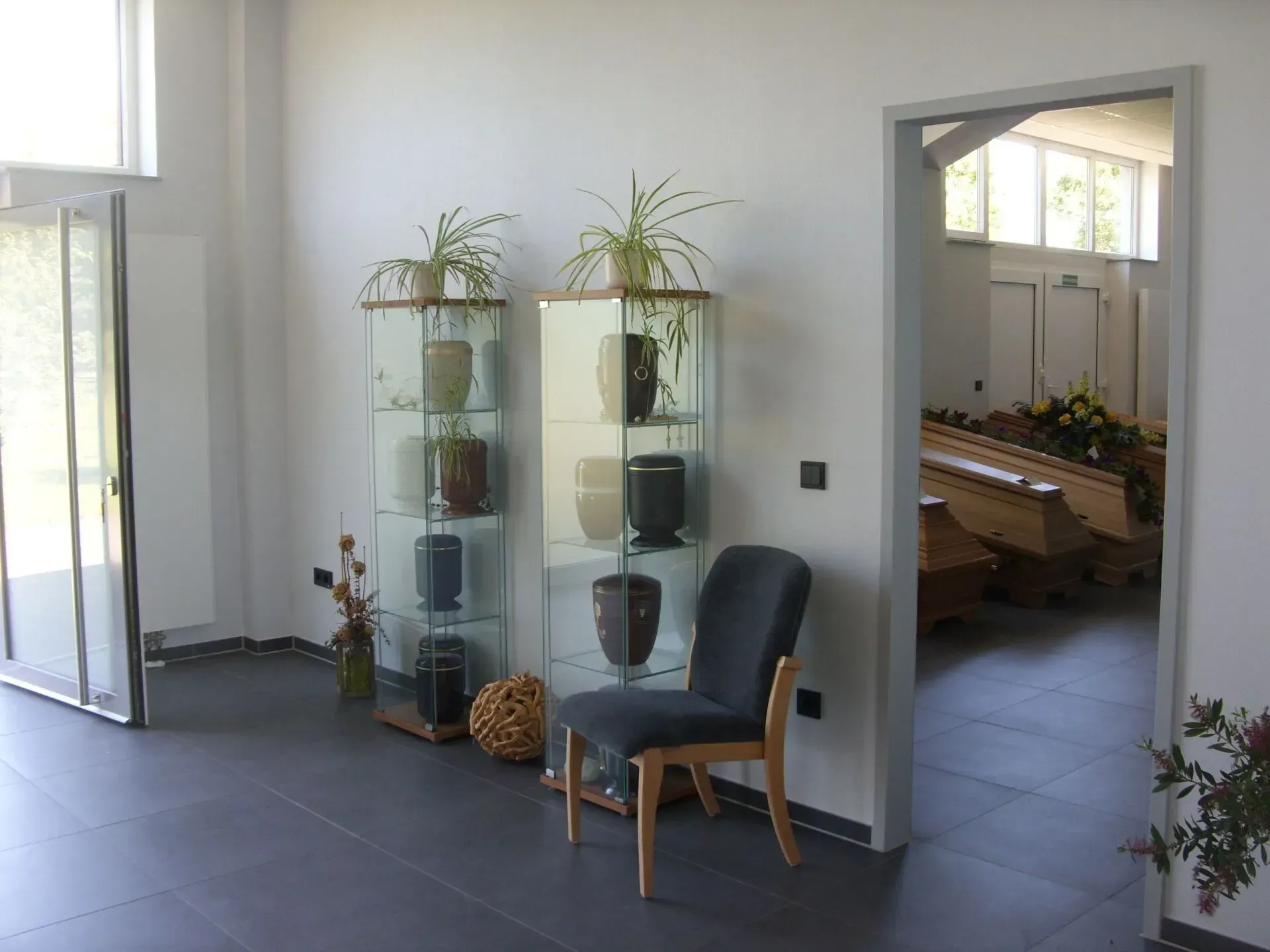 Innenansicht eines Bestattungsinstituts mit Urnen in Vitrinen, einem Stuhl und dem Eingang zu einem Trauerraum.