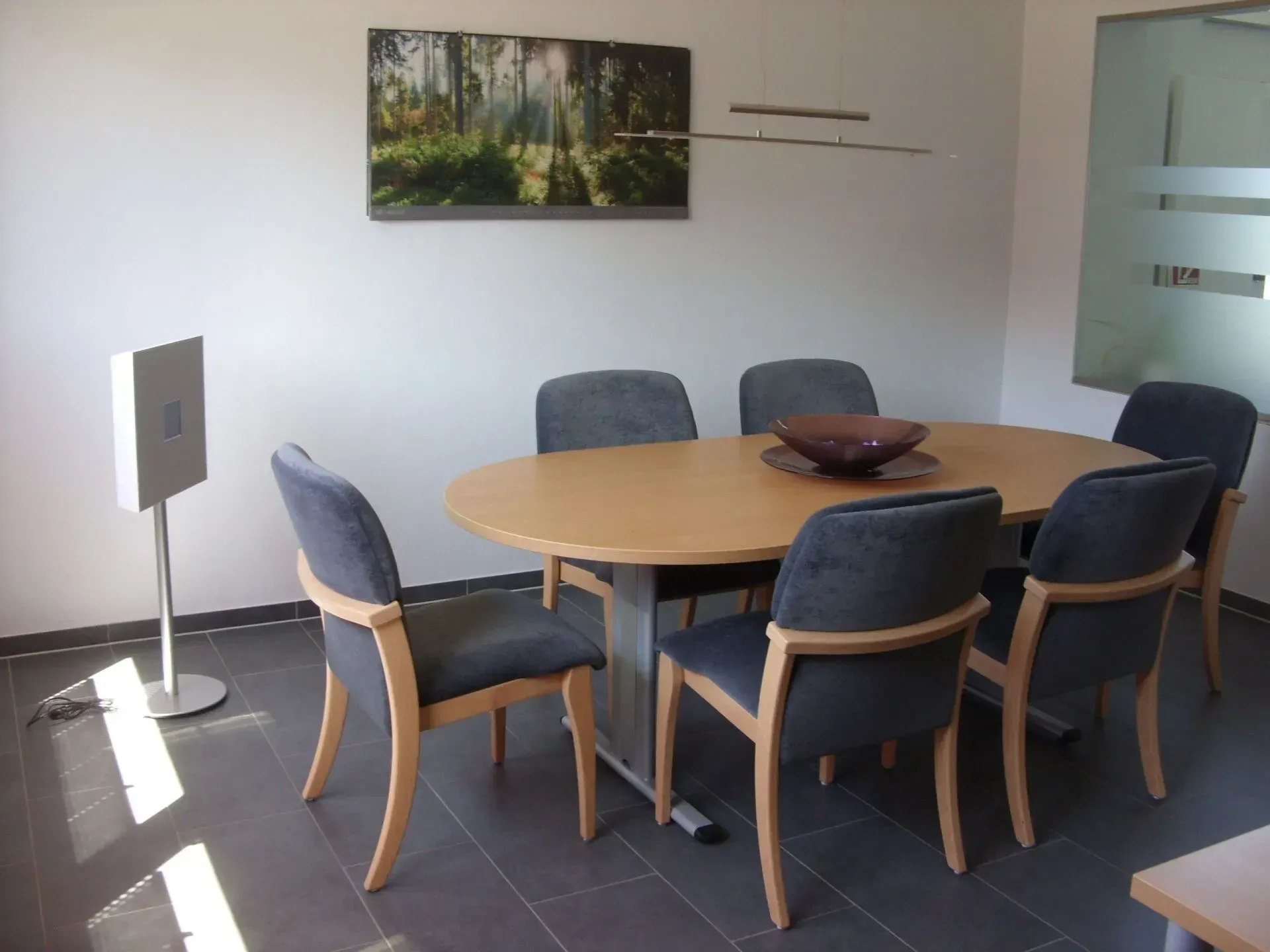 Ovaler Esstisch mit sechs Stühlen, einer Schale als Tischdekoration und Kunstwerken an der Wand in einem hellen Raum.