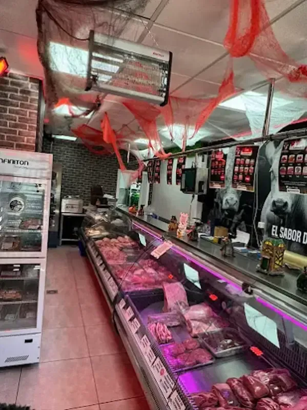 Interior de carnicería con una vitrina larga llena de carne y decoraciones rojas y blancas en lo alto.
