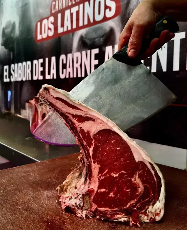 Un gran filete de costilla crudo con hueso cortado con un cuchillo de carnicero; fondo de tienda.