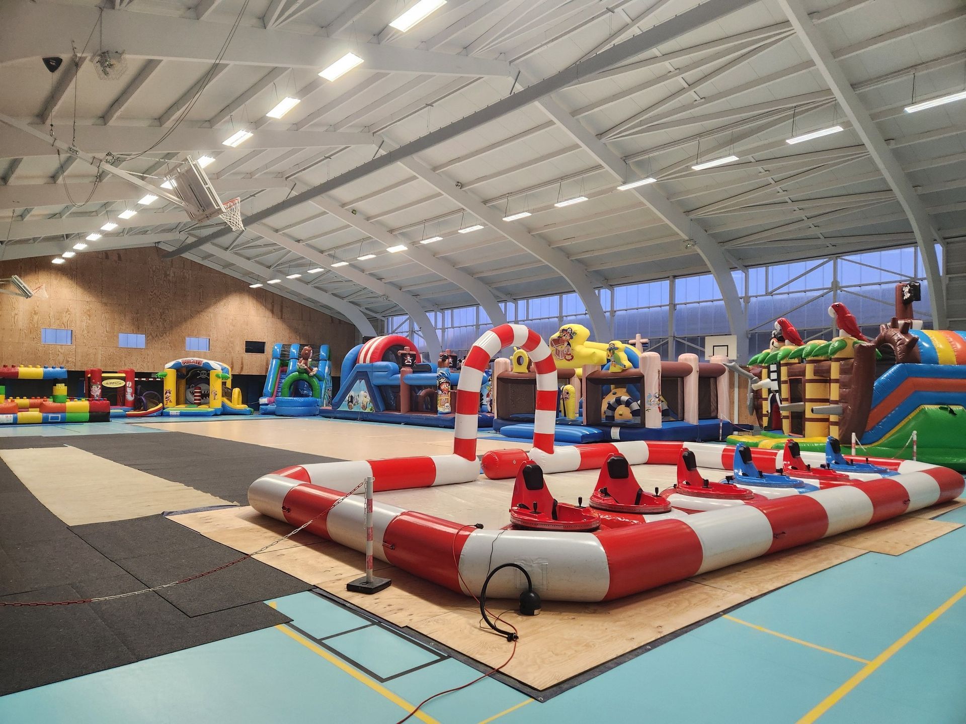 Aire de jeux gonflable intérieure avec diverses structures colorées et un espace pour bateaux tamponneurs.