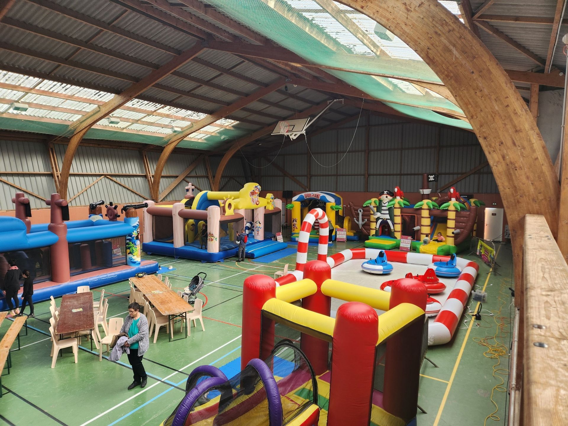 Aire de jeux intérieure avec diverses structures gonflables, tables et personnages ; sol vert clair.