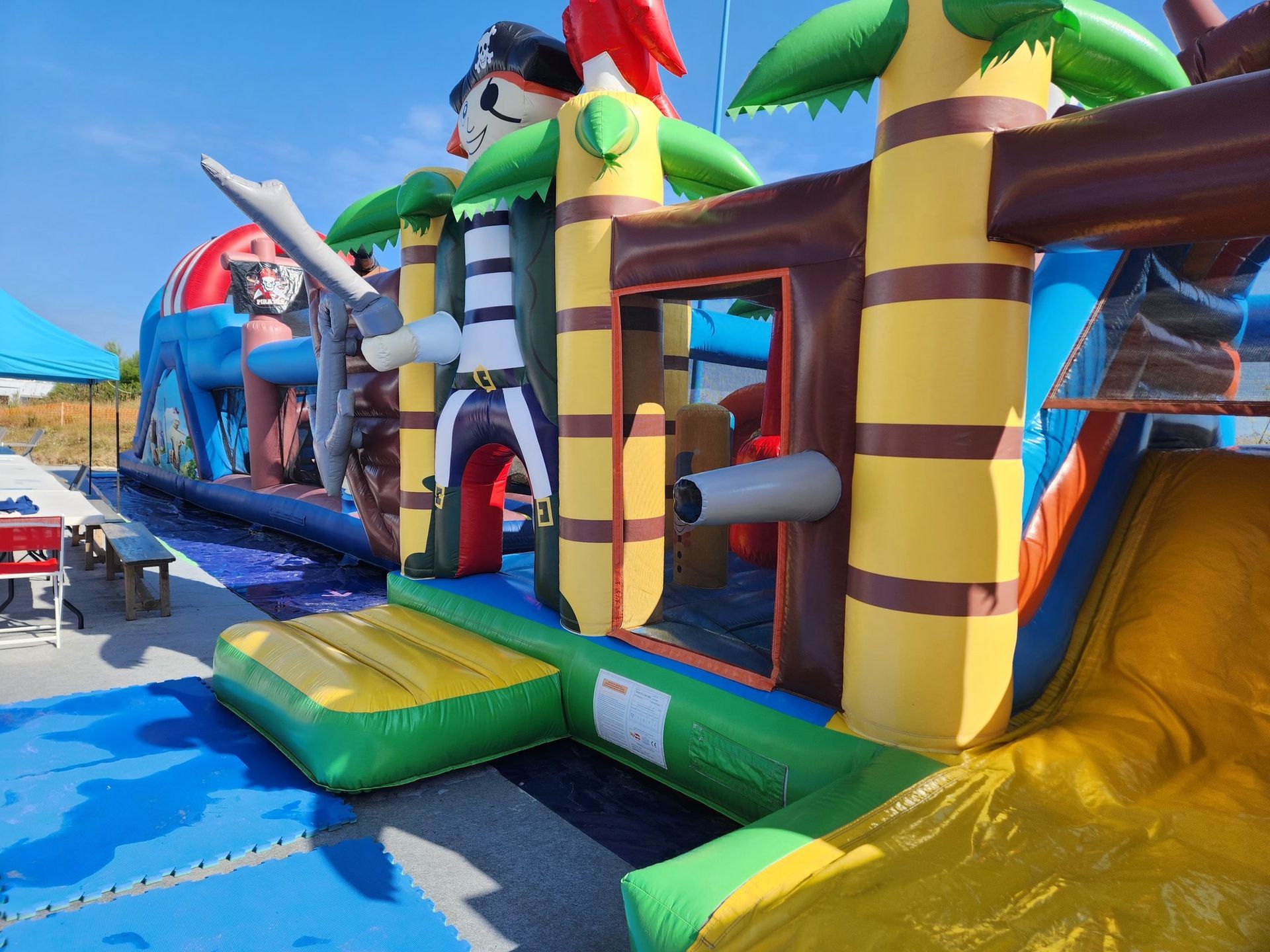 Maison gonflable d'extérieur sur le thème des pirates, avec toboggan et piscine. Couleurs vives : jaune, bleu, vert et rouge.