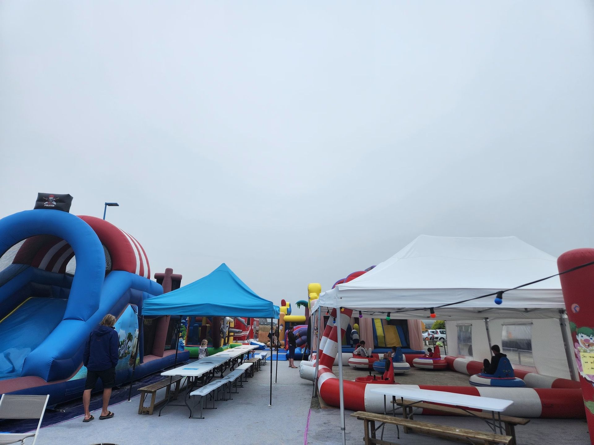 Aire de jeux gonflable extérieure avec toboggans, tables et tentes sous un ciel nuageux.