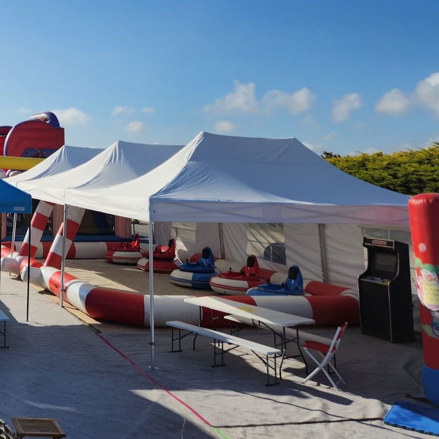 Scène de carnaval en plein air avec tentes blanches, autos tamponneuses et jeux d'arcade. Ciel bleu.