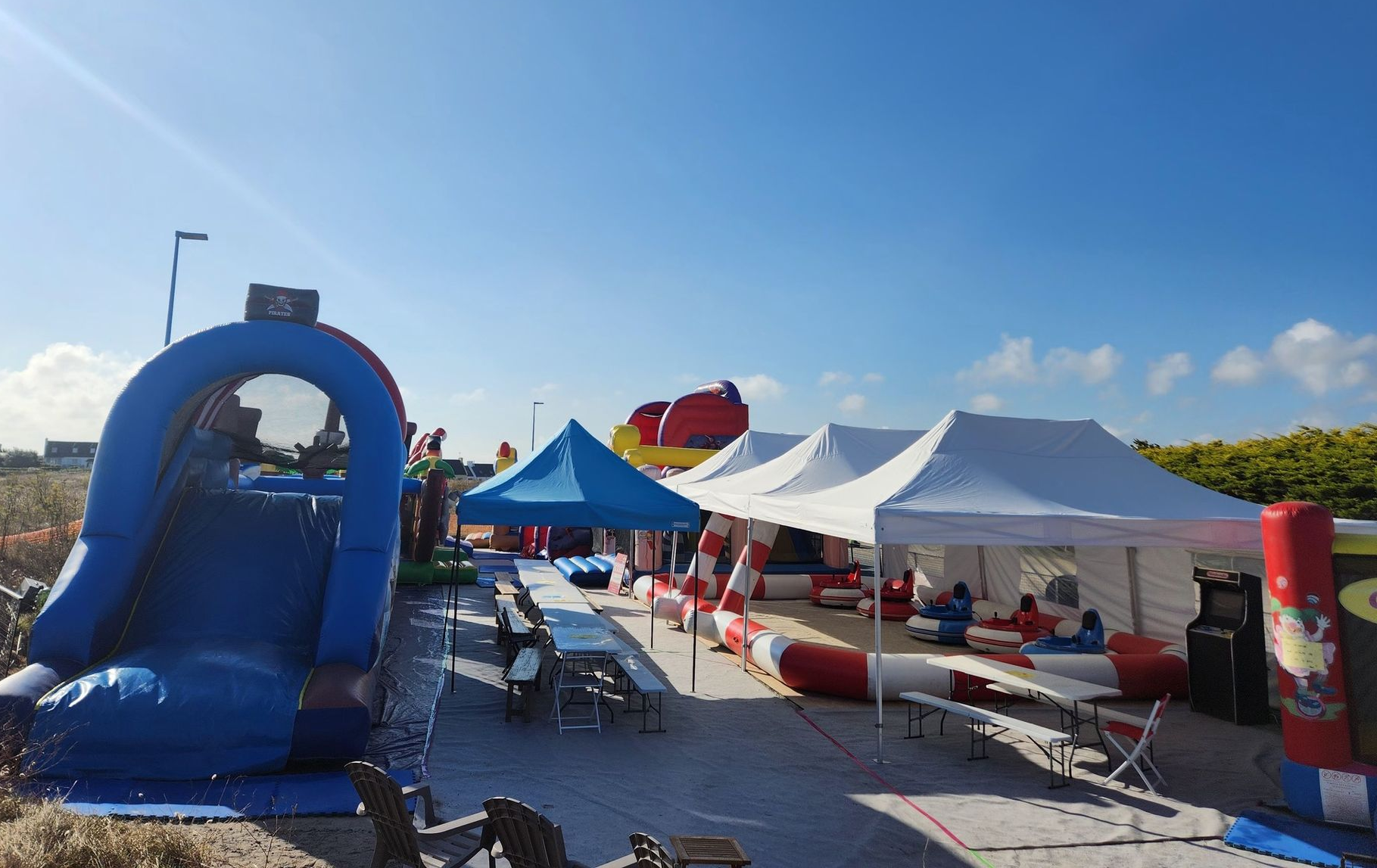 Événement en plein air avec toboggan gonflable, tentes et tables sous un ciel bleu.