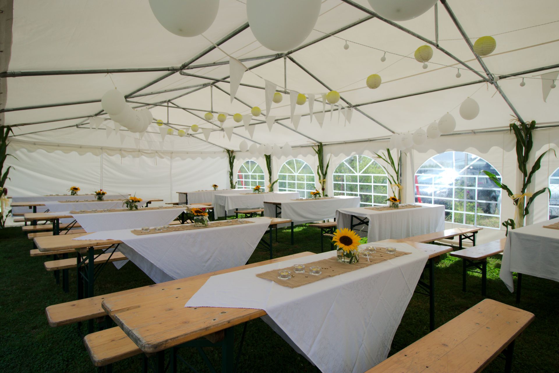 À l'intérieur d'une tente blanche, de longues tables dressées avec des nappes blanches, des tournesols et des décorations ; pour une fête.