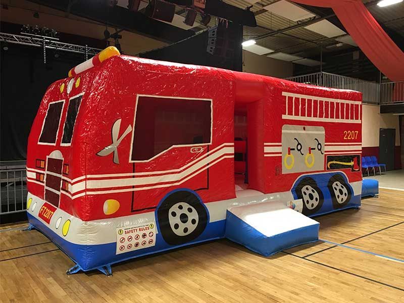 Maison de jeu gonflable en forme de camion de pompiers rouge dans un gymnase.
