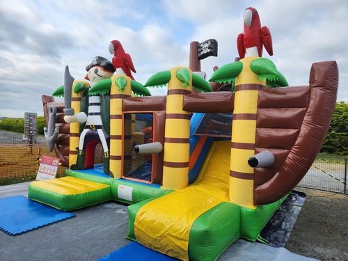 Maison gonflable sur le thème des pirates avec toboggan, perroquets et drapeau, installée à l'extérieur.