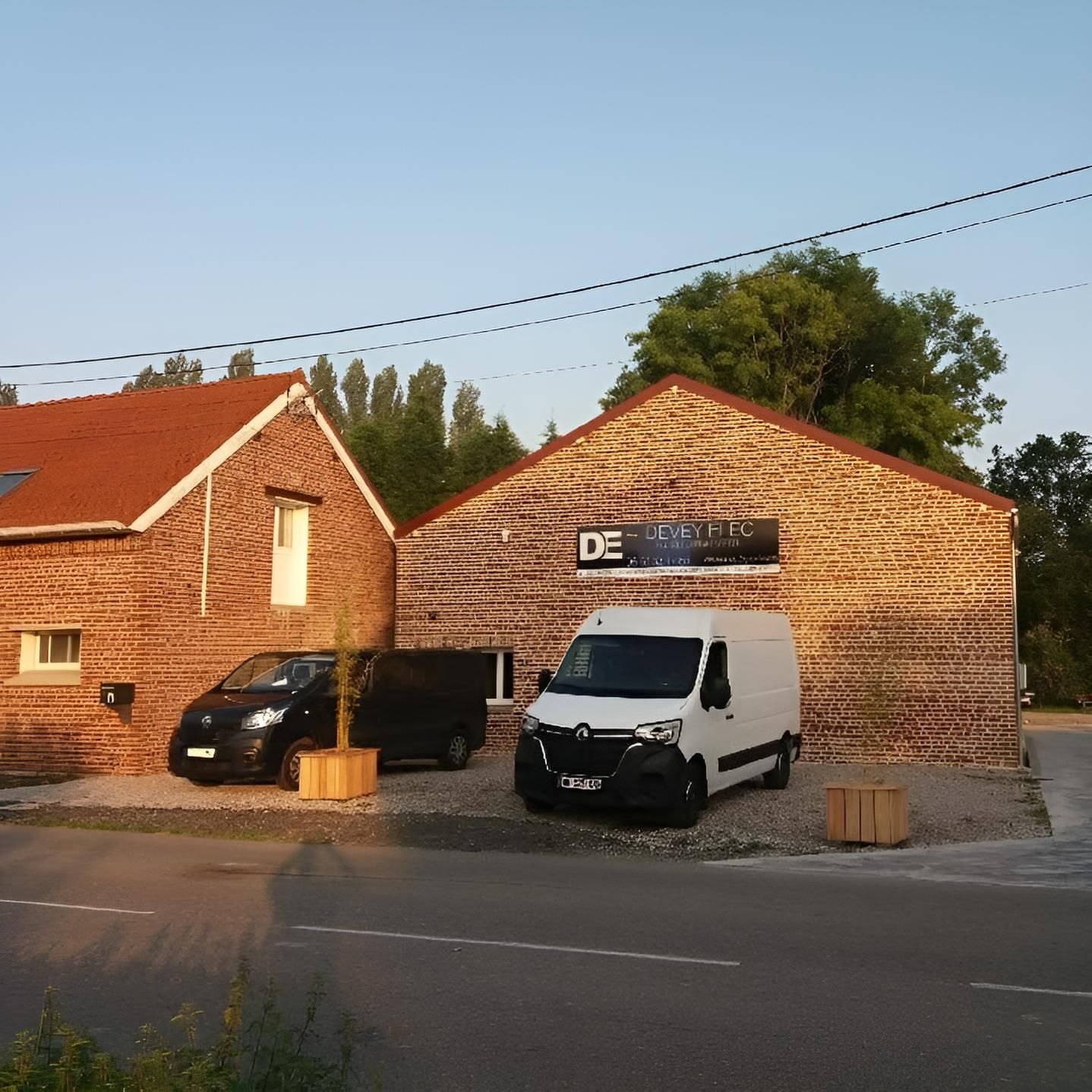 Deux camionnettes garées à côté d'un bâtiment en briques portant une enseigne d'entreprise, en bord de route.