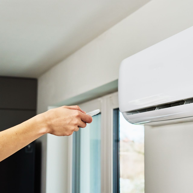 Main pointant une télécommande vers un climatiseur mural près d'une fenêtre