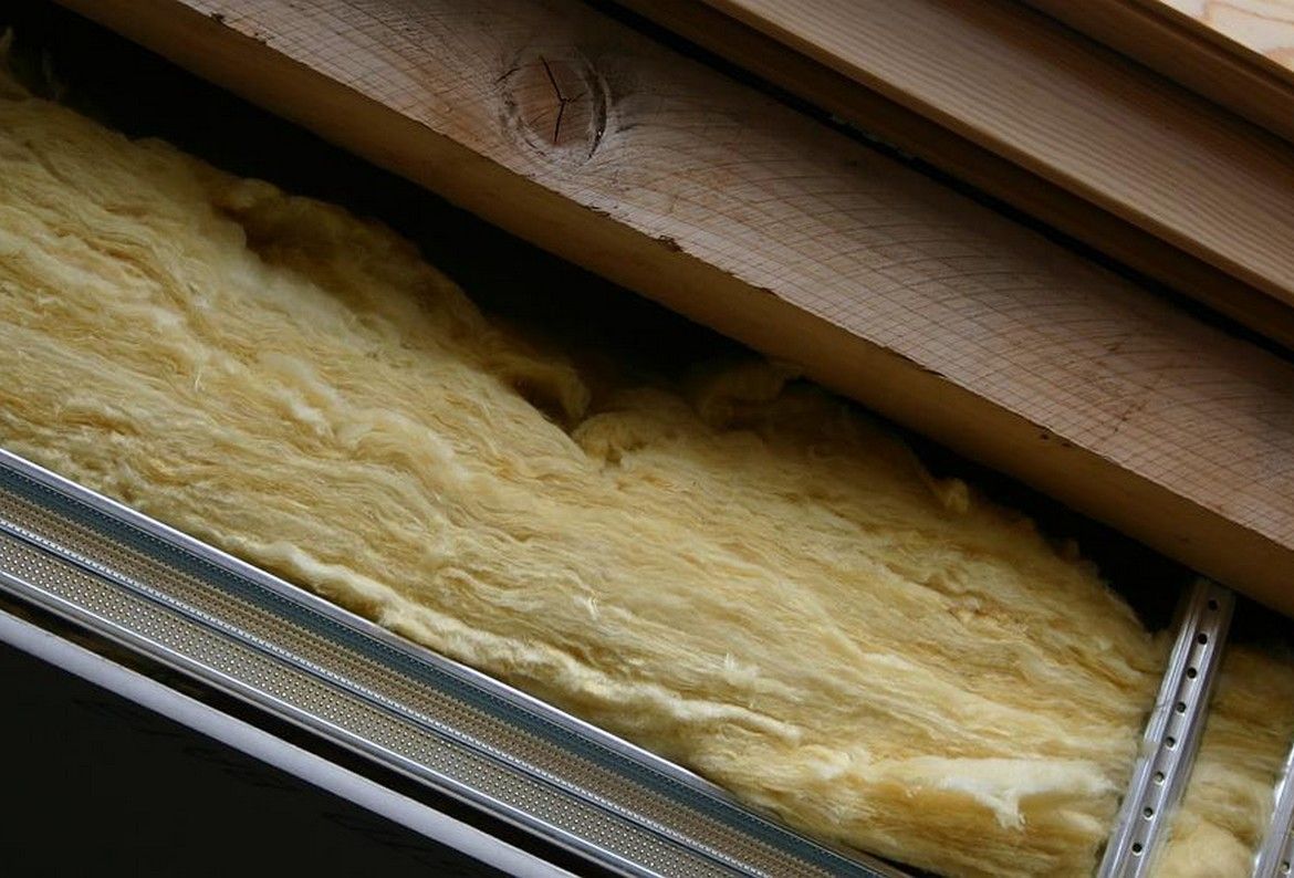 Isolation en fibre de verre jaune insérée entre une ossature en bois et des rails métalliques pour plaques de plâtre.