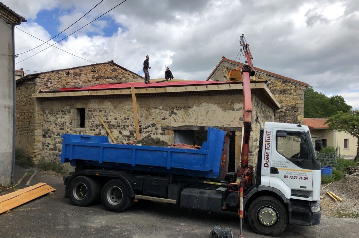 Des ouvriers travaillent sur le toit d'un bâtiment, un camion-grue stationné devant pour un chantier de construction.