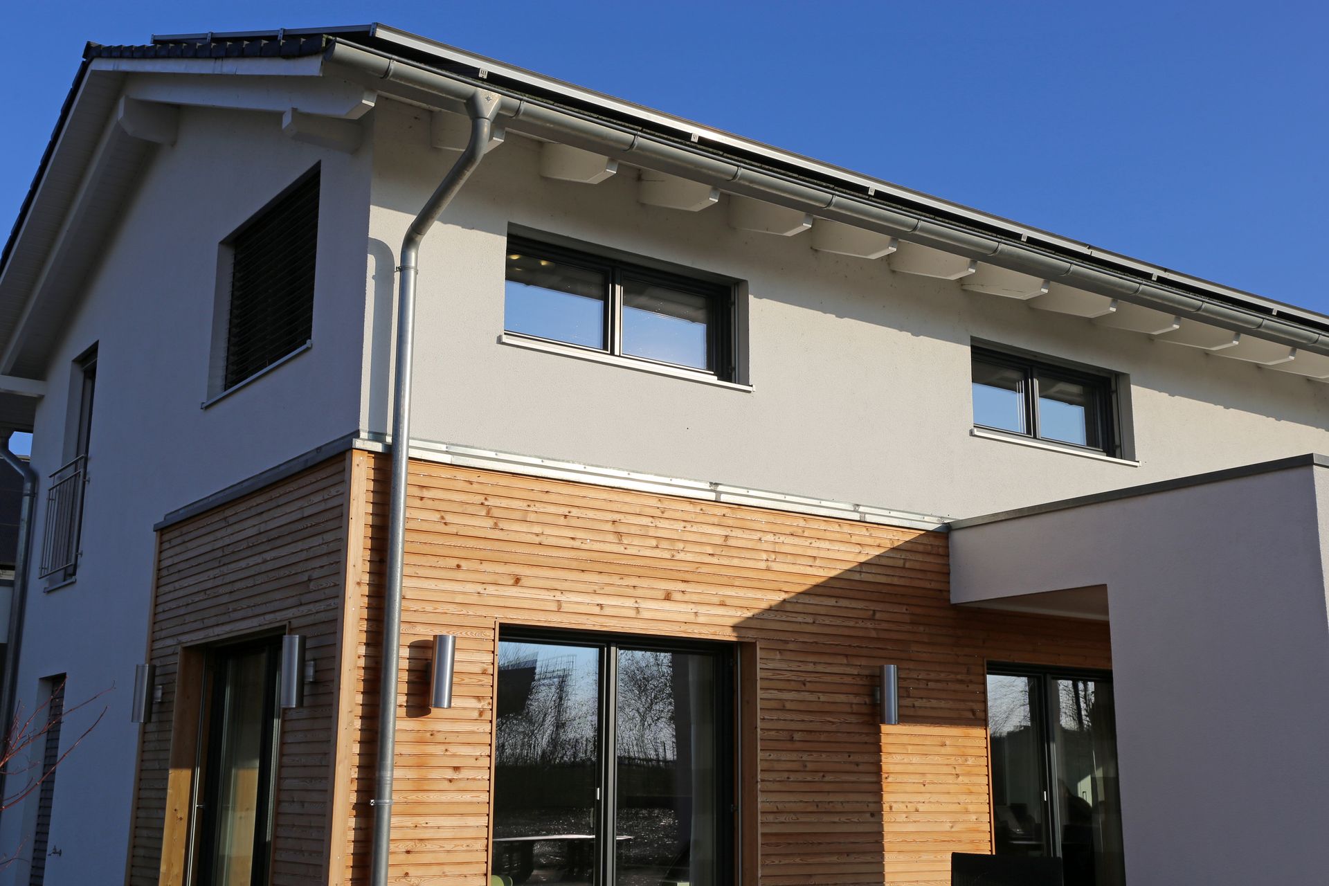 Une maison moderne à deux étages, des murs extérieurs beiges et un bardage en bois horizontal au rez-de-chaussée.