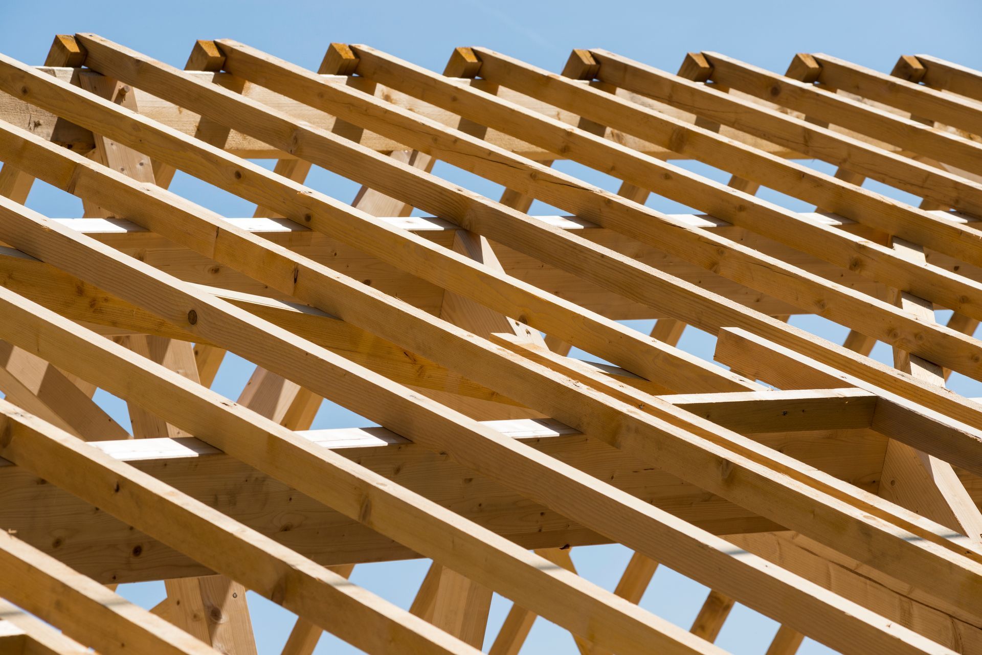 Des chevrons de charpente en bois soutiennent la structure d'un bâtiment qui se détache sur un ciel bleu limpide.