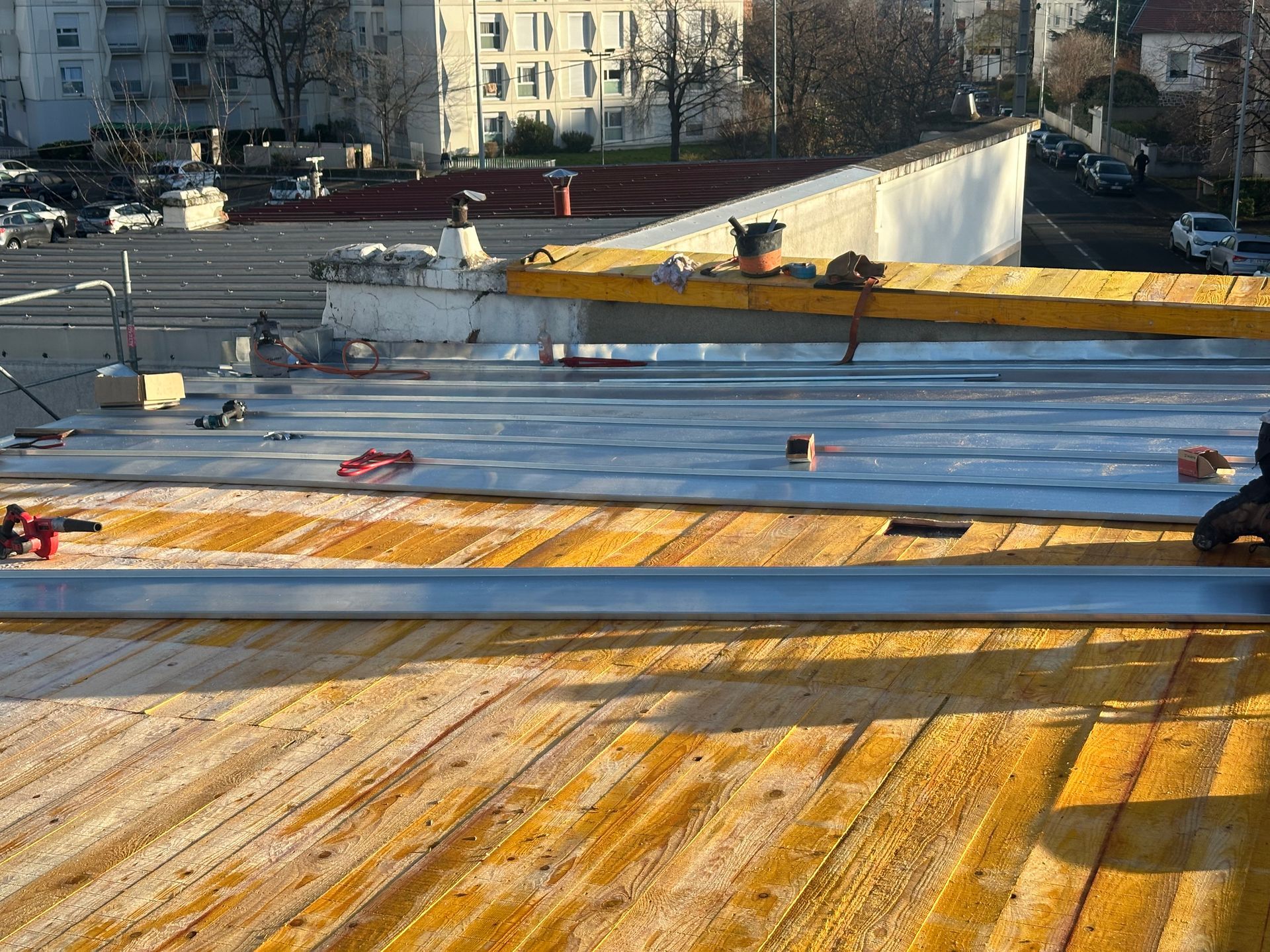 Vue d'un chantier de construction montrant un toit en bois partiellement recouvert de tôles métalliques.