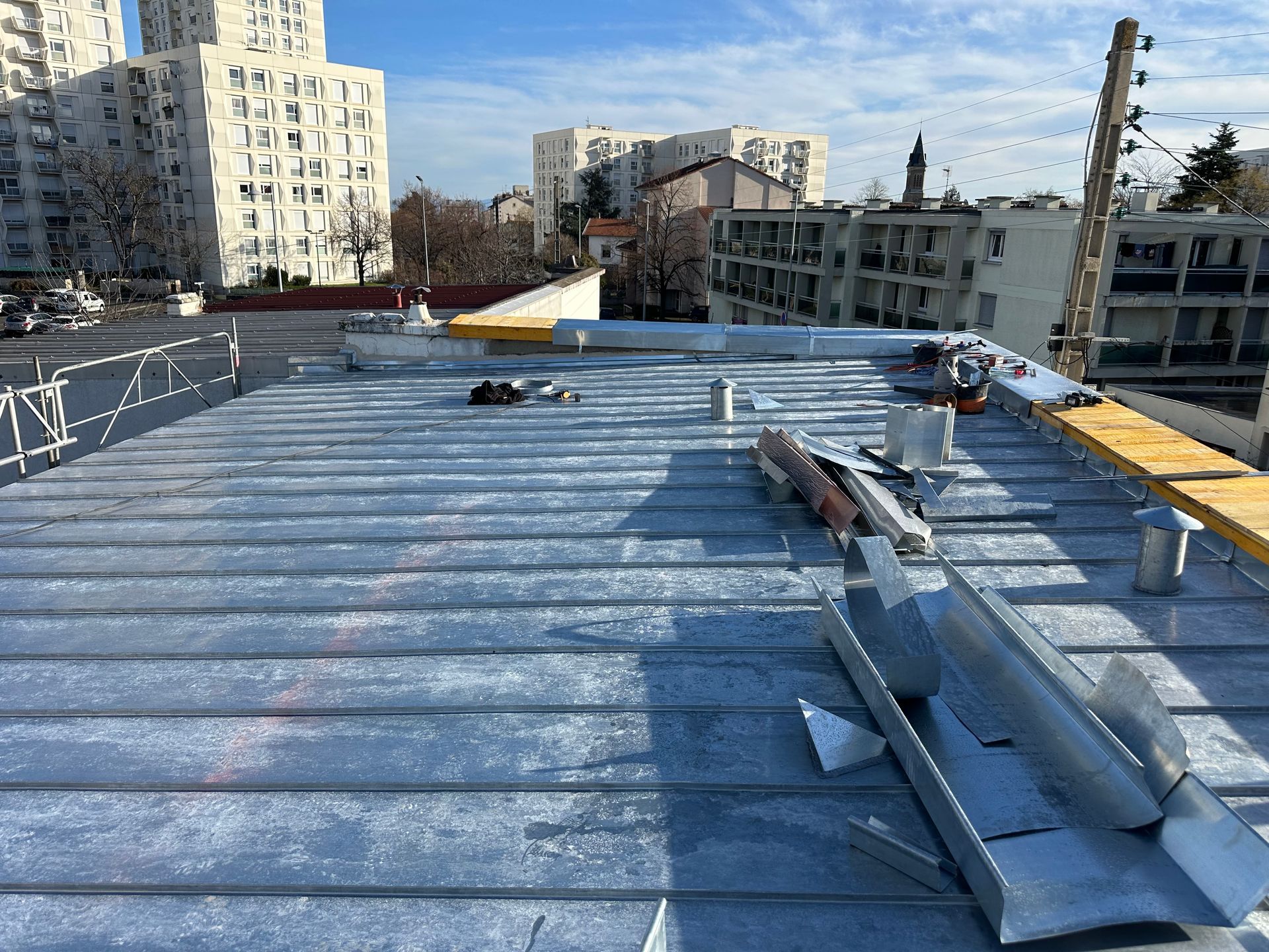 Un toit plat recouvert de panneaux de toiture métalliques à joints debout, des matériaux de construction et des immeubles.