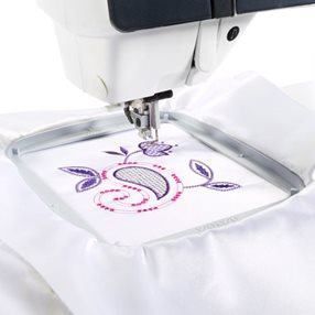 Una máquina de coser está bordando una flor sobre una tela blanca.