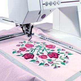 Una máquina de coser está bordando un diseño floral sobre una tela rosa.