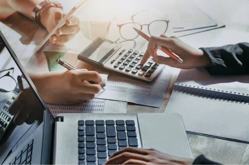 Hände, die Taschenrechner und Laptops bedienen, um einen Schreibtisch mit Finanzdokumenten und Diagrammen.