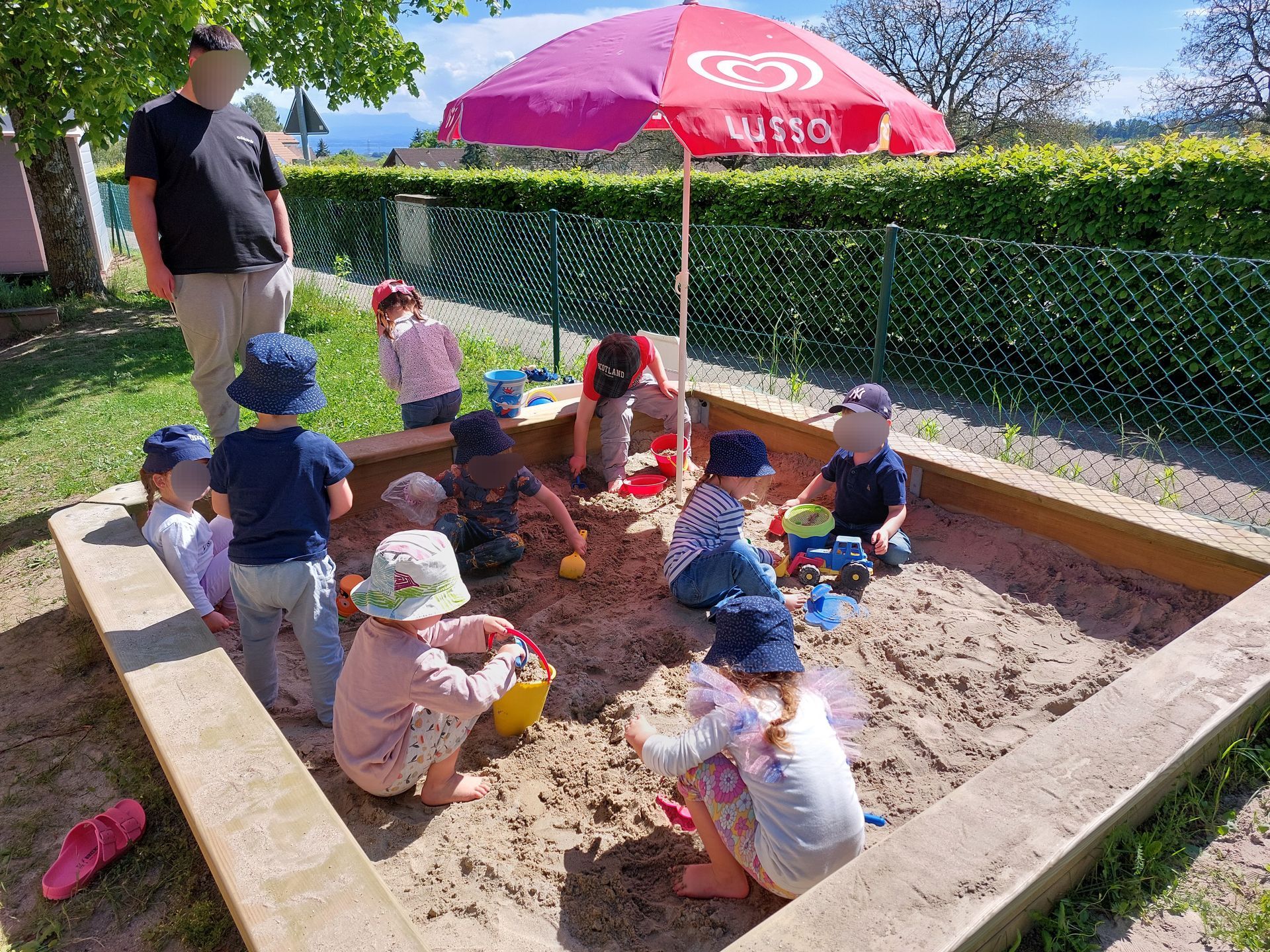 Une salle de classe où des enfants sont rassemblés autour de deux tables, en train de bricoler avec des feuilles et de la colle près d'un sapin de Noël.