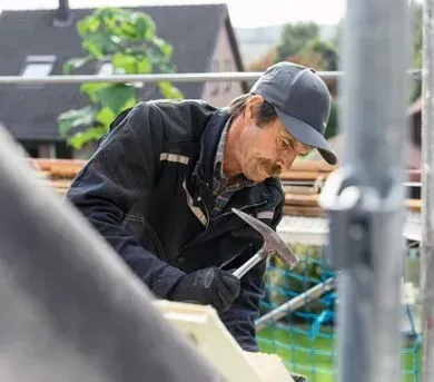 Dachdecker sitzt auf einem Dach und deckt es mit neuen Dachziegeln