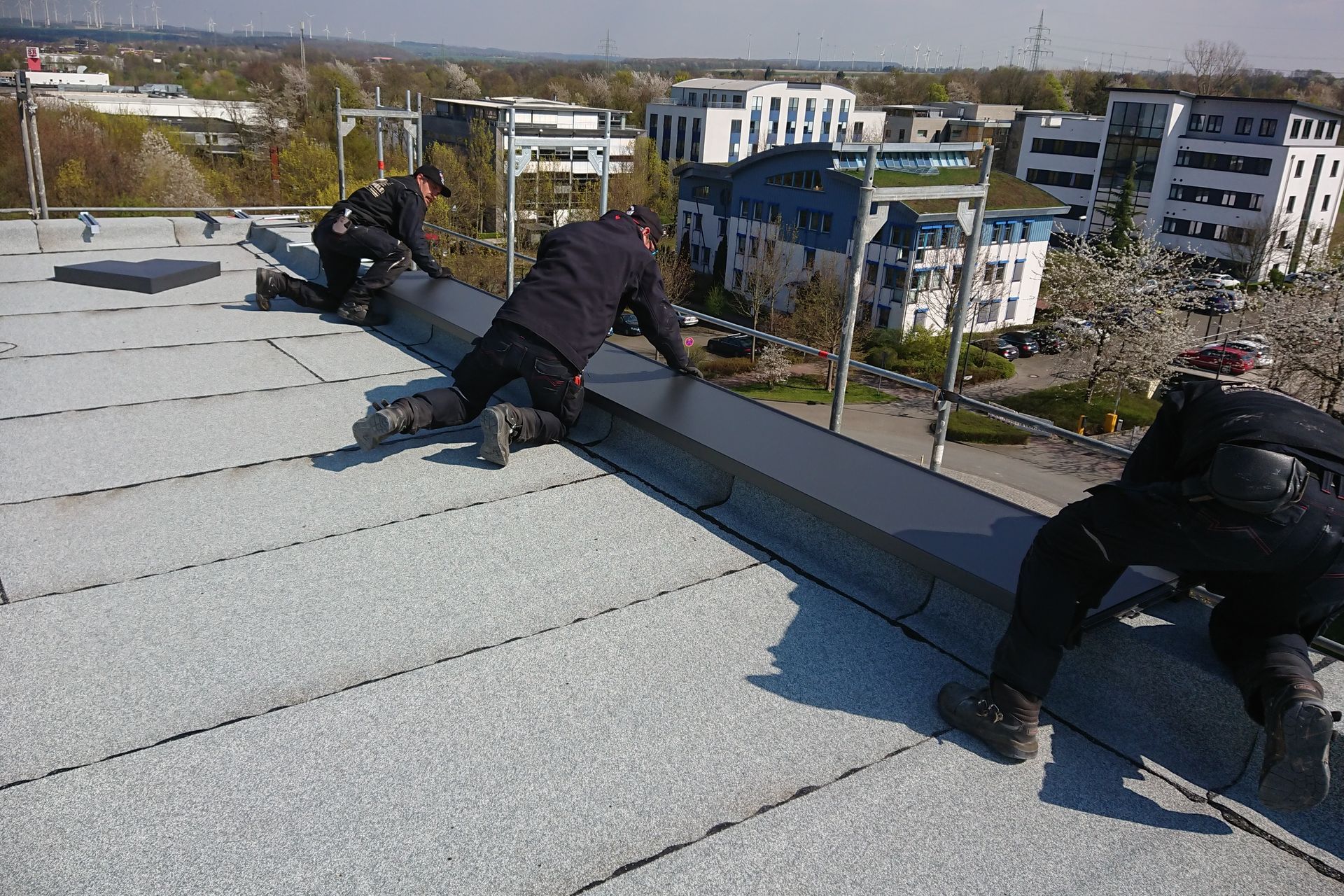Flachdach wird von drei Dachdeckern bearbeitet