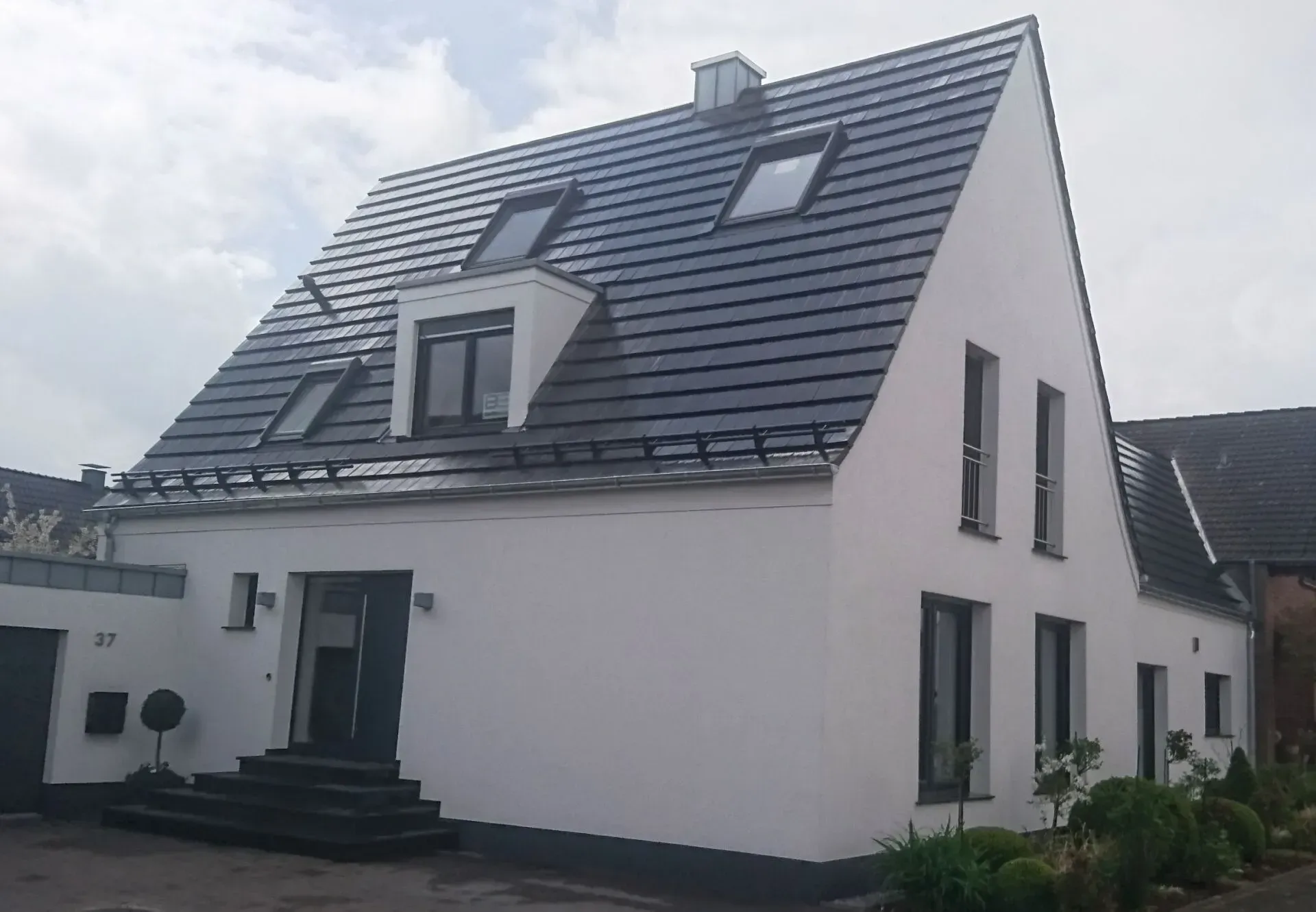 Modernes weißes Haus mit dunkel gedecktem Dach und Dachfenstern