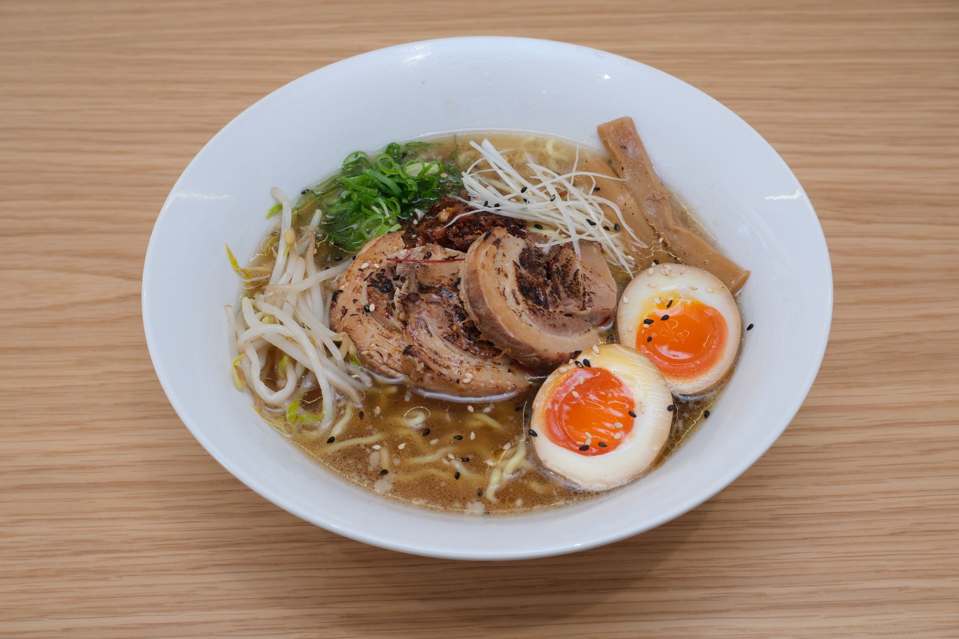 Ramen em uma tigela branca, coberto com barriga de porco, ovos, brotos de feijão e brotos de bambu.