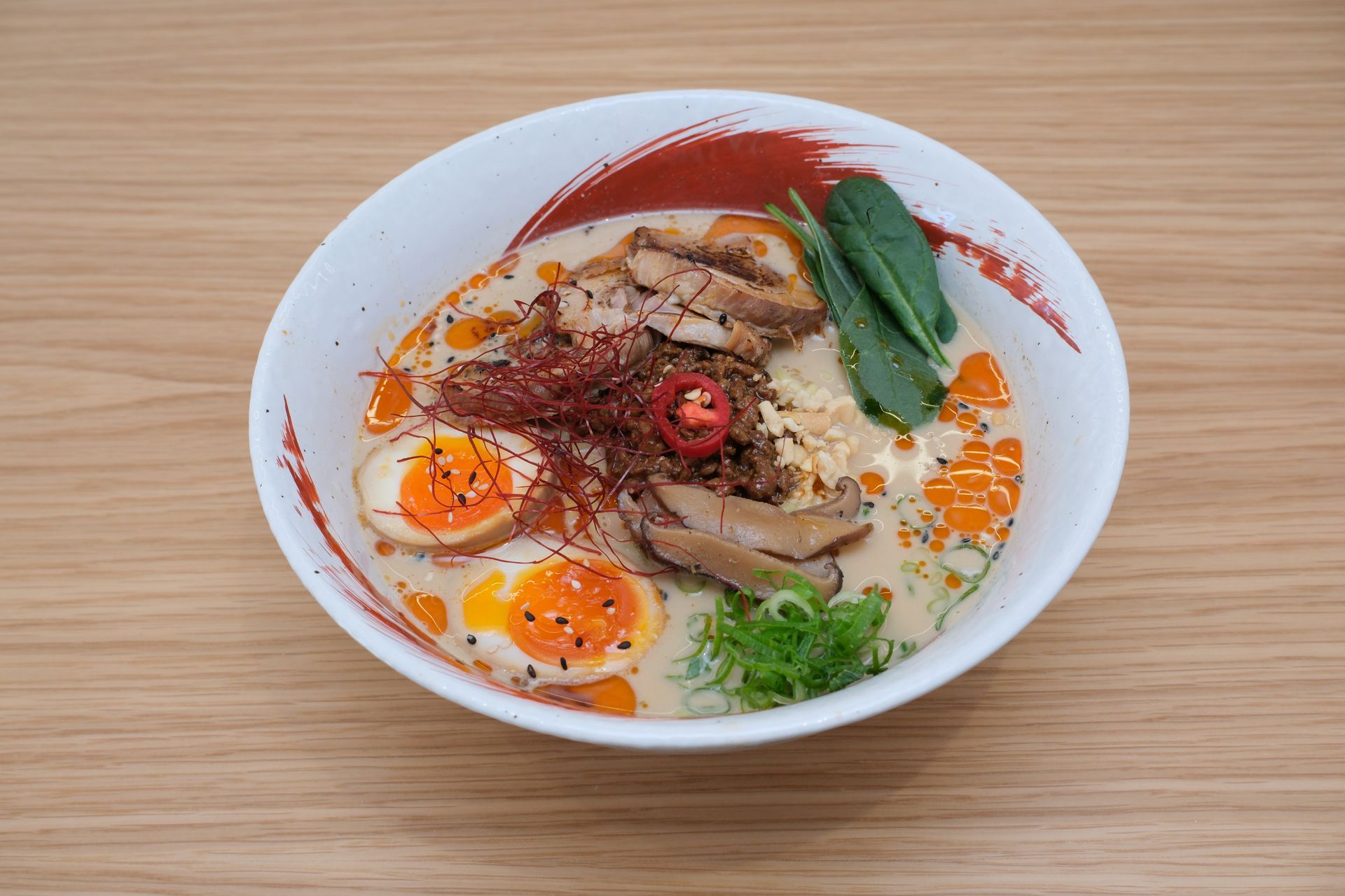 Tigela de ramen com ovos, carne, vegetais e flocos de pimenta vermelha em uma tigela branca