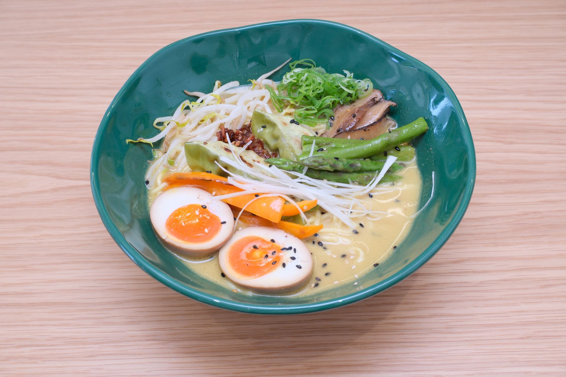 Ramen em uma tigela verde com ovos cozidos, vegetais e brotos.