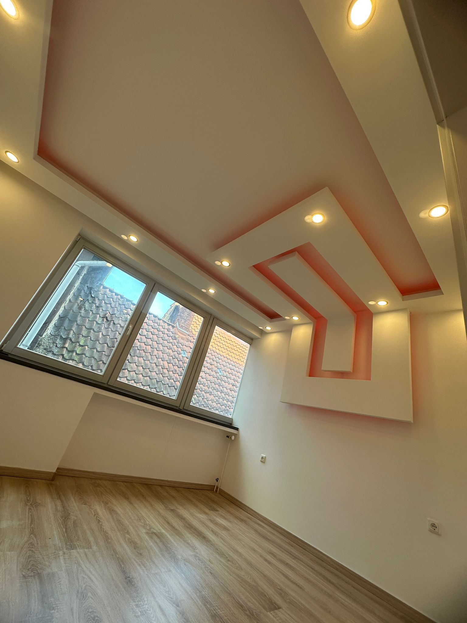 Ein leerer Raum mit einer rosa Decke und einem großen Fenster.