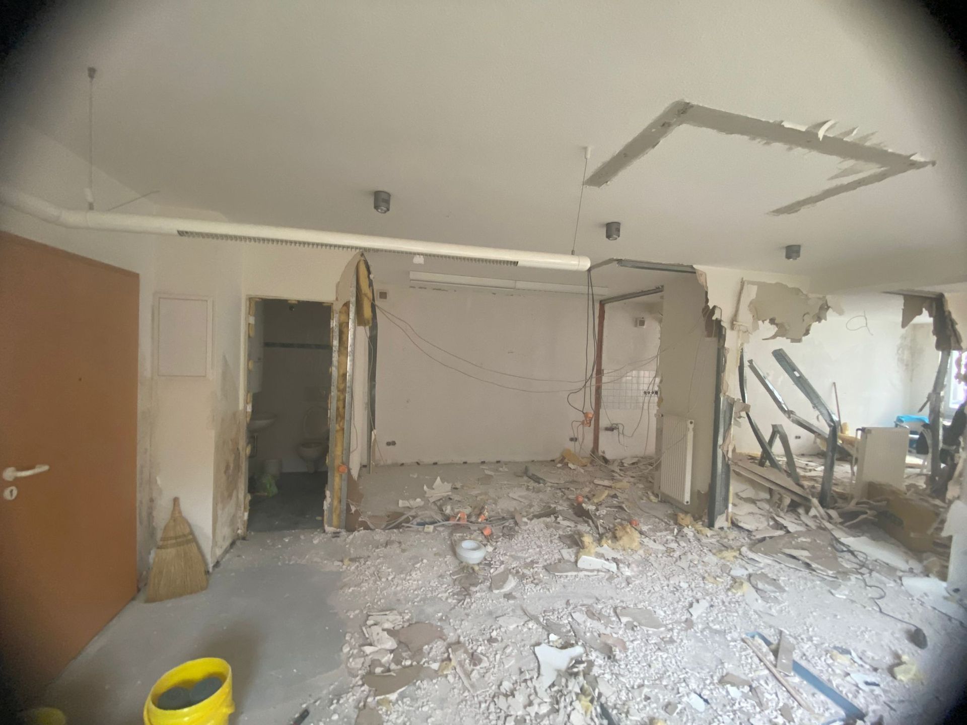 Ein Raum mit einer kaputten Wand und einem gelben Eimer auf dem Boden.